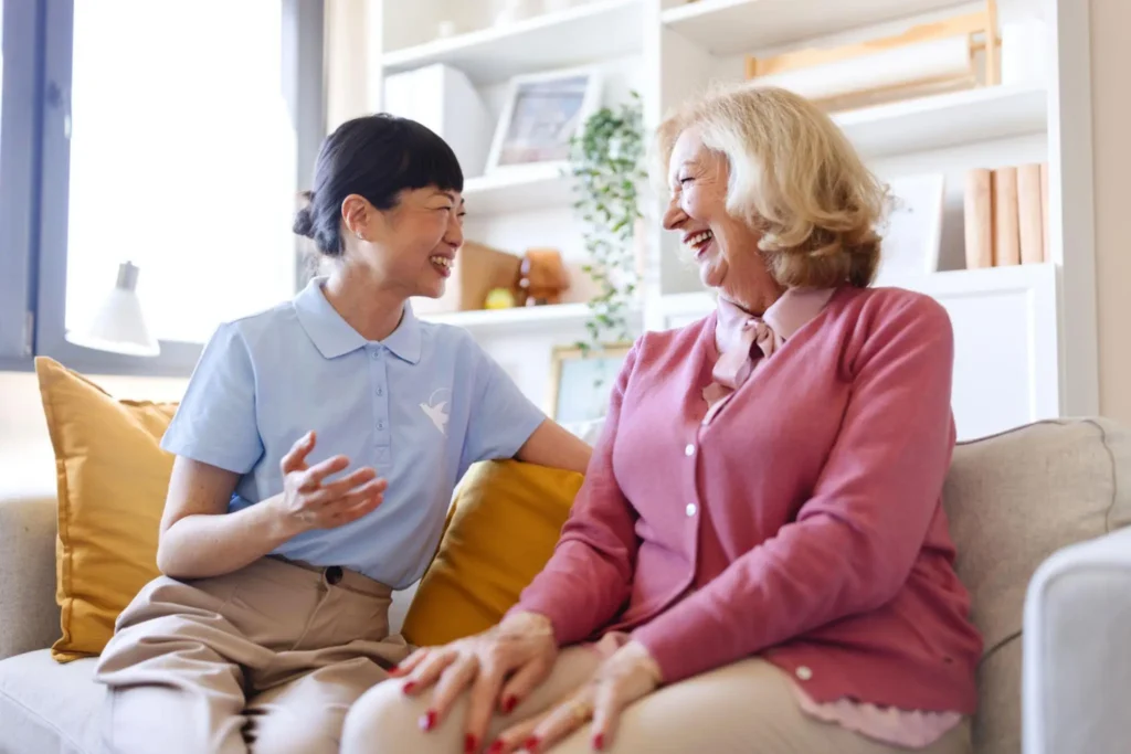 Senior smiling while talking with a caregiver at home | Rose Hill Care